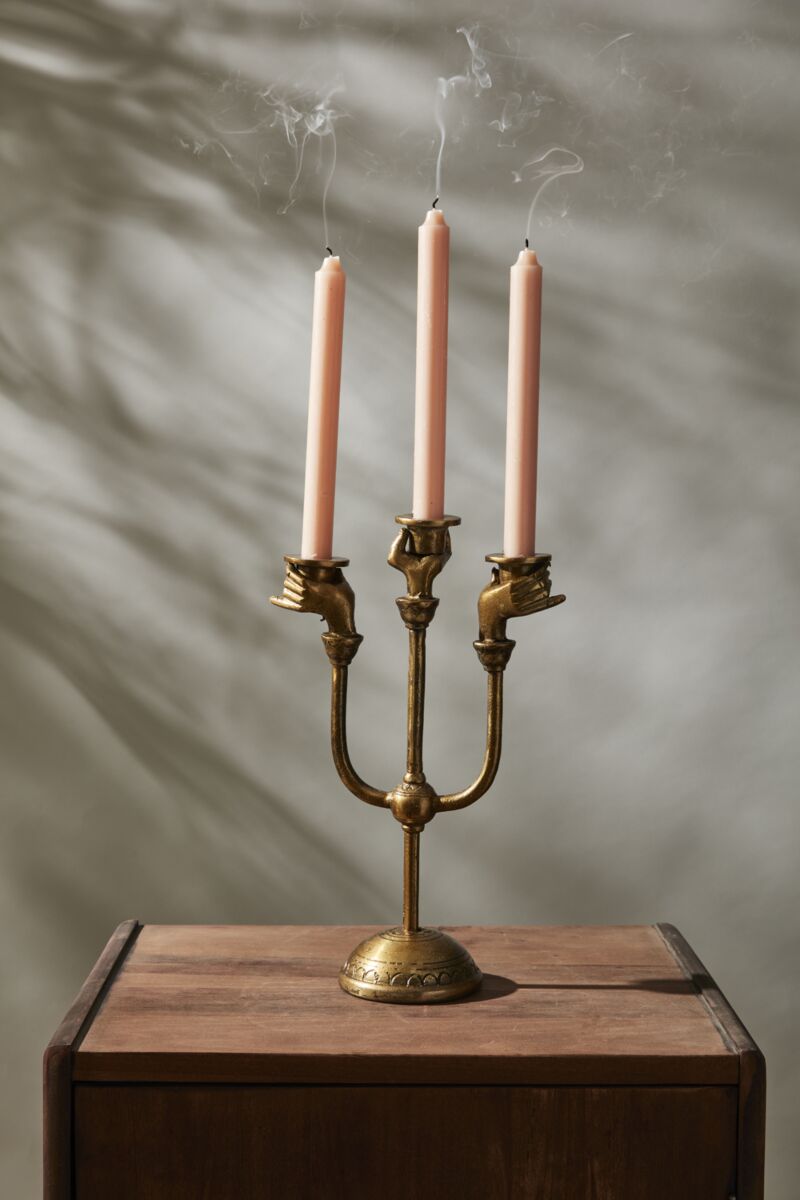 The Accent Decor Haunted Hands Candelabra features three just-extinguished pink candles, with smoke curling from the wicks—a bewitching Halloween table accent set on wood against a softly shadowed neutral background.