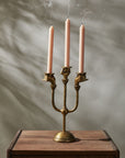 The Accent Decor Haunted Hands Candelabra features three just-extinguished pink candles, with smoke curling from the wicks—a bewitching Halloween table accent set on wood against a softly shadowed neutral background.