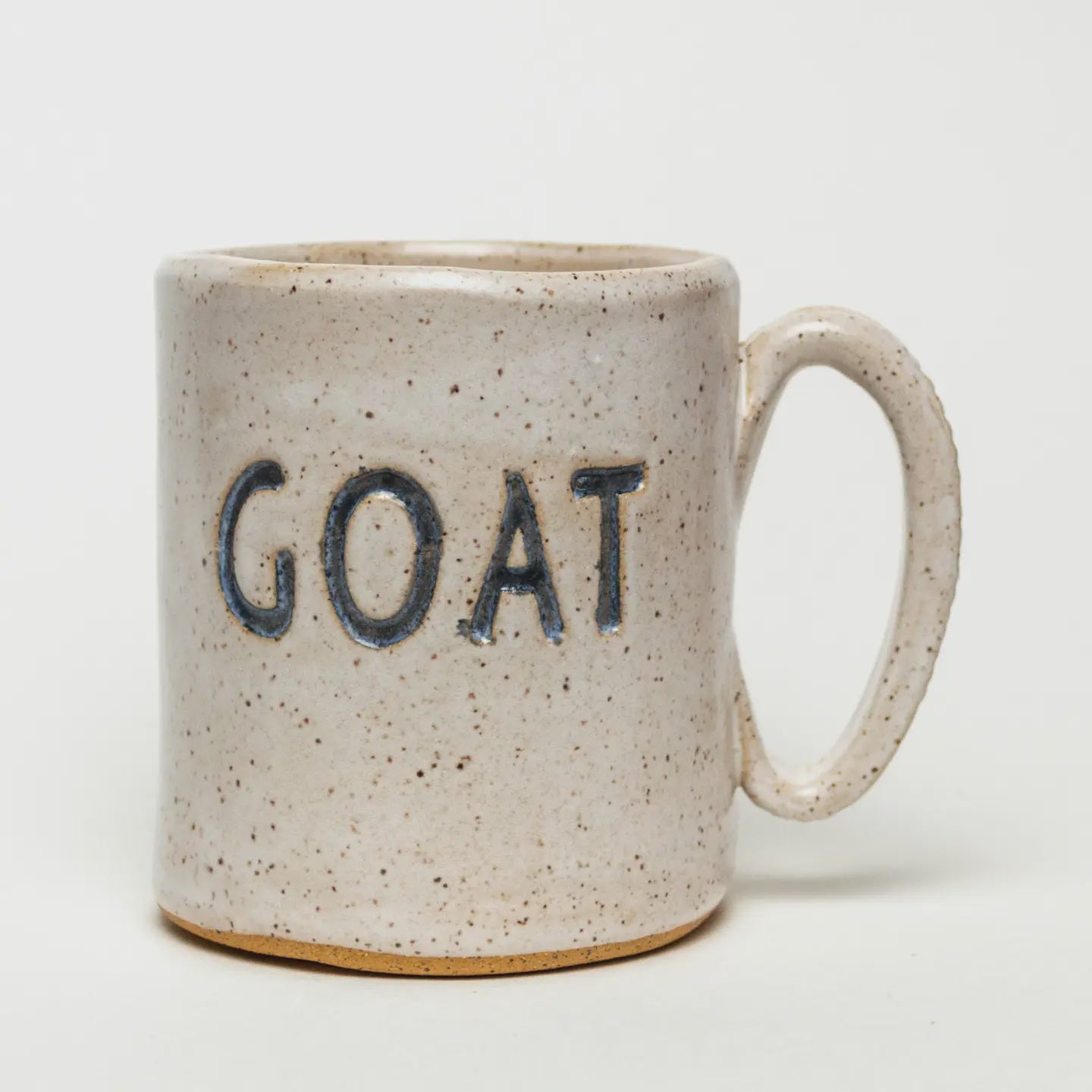 A handmade ceramic mug from Faire, featuring a speckled beige finish and blue "GOAT" lettering, set against a plain white background.