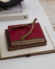 The Wishbone Sculpture by Accent Decor sits atop two stacked red hardcover books on an open book, all placed on a white surface. A white book and a decorative bowl are partially visible nearby.