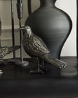 The Nevermore Figurine by Accent Decor stands on a dark shelf before a matte black ceramic pitcher, surrounded by other dark-toned decor for a subtle haunted vibe.