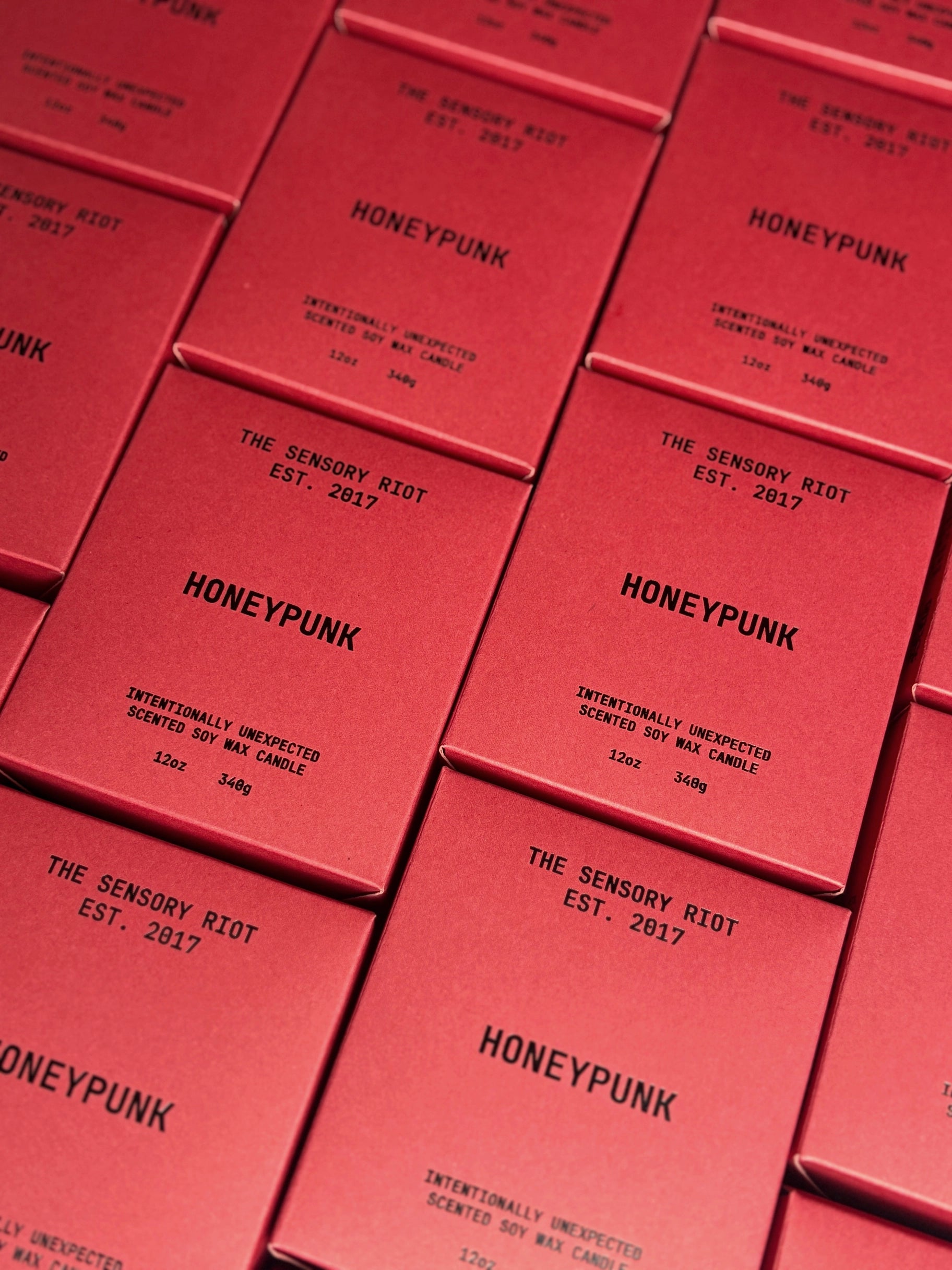 Several HONEYPUNK 12 oz candles by Faire are arranged in a grid, each box labeled with "The Sensory Riot Est. 2017" and "Intentionally Unexpected Spiced Honey Scented Soy Wax Candle.