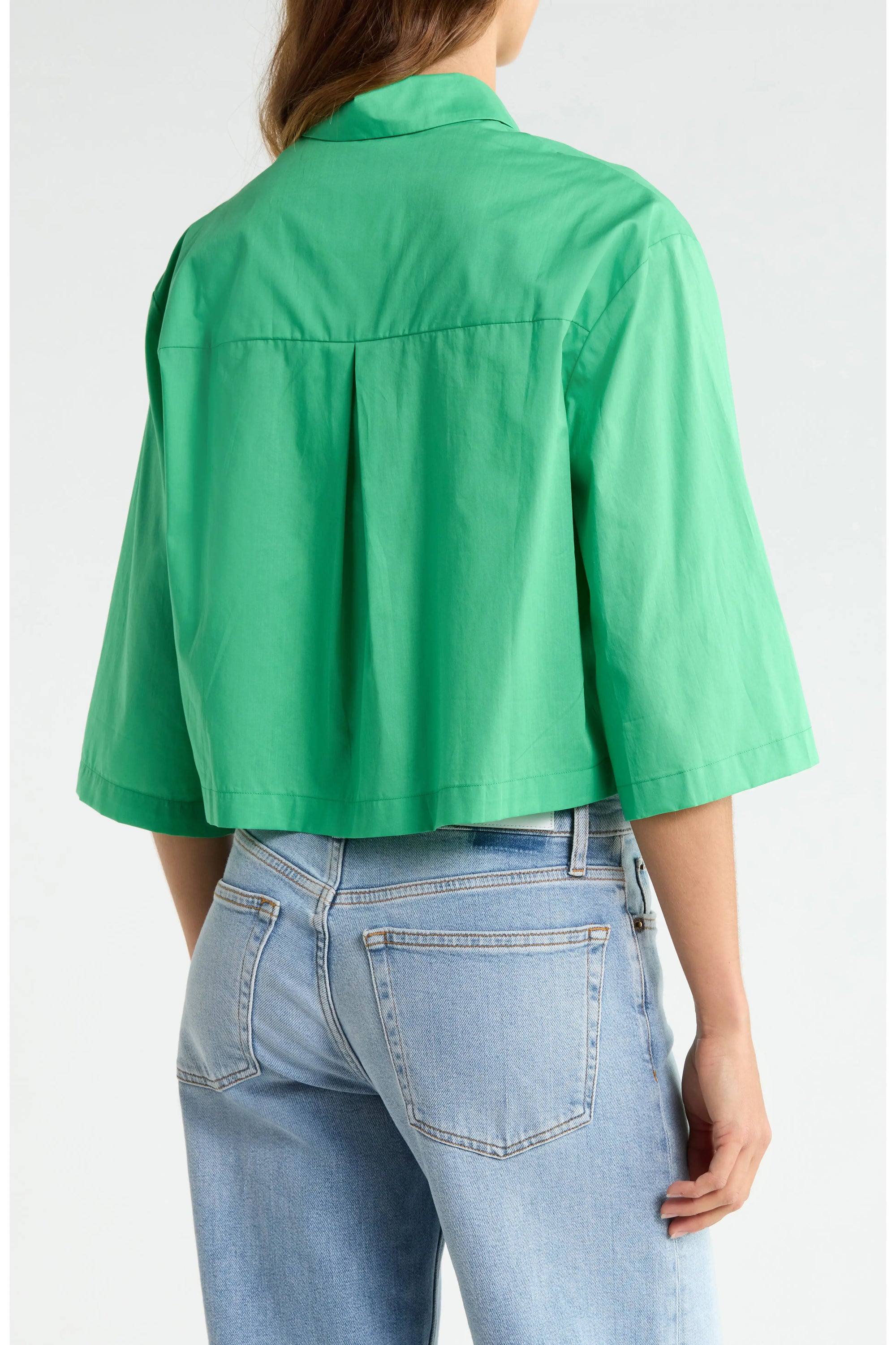 A person is seen from behind wearing Cissa's The PIXIE Shirt—a loose, bright green cotton poplin top with a boxy fit and short sleeves—paired with light blue high-waisted jeans, highlighting the shirt's structured back and sleeves.