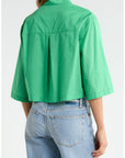 A person is seen from behind wearing Cissa's The PIXIE Shirt—a loose, bright green cotton poplin top with a boxy fit and short sleeves—paired with light blue high-waisted jeans, highlighting the shirt's structured back and sleeves.