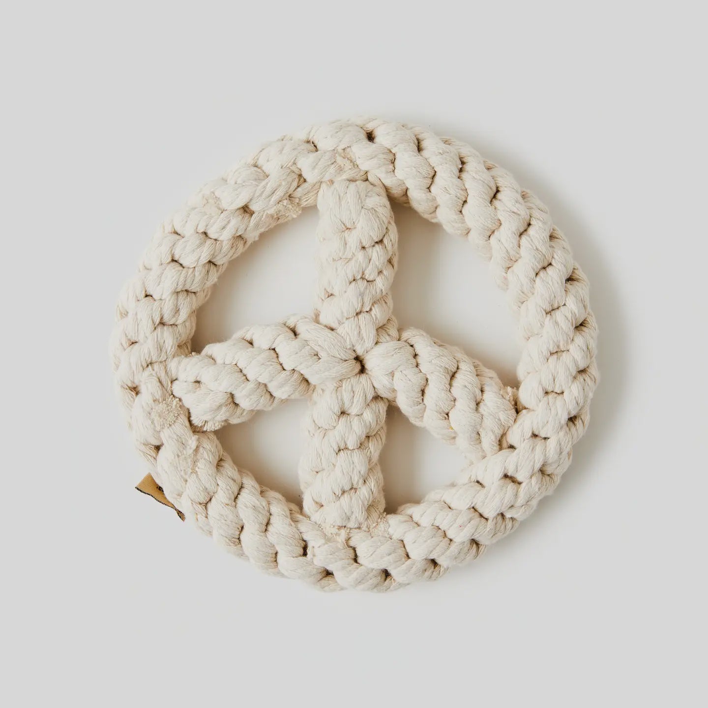 A beige, braided Peace Sign Dog Toy from Faire, made of rough natural fibers, shaped into a peace symbol against a plain light background, promotes animal welfare through mindful design.