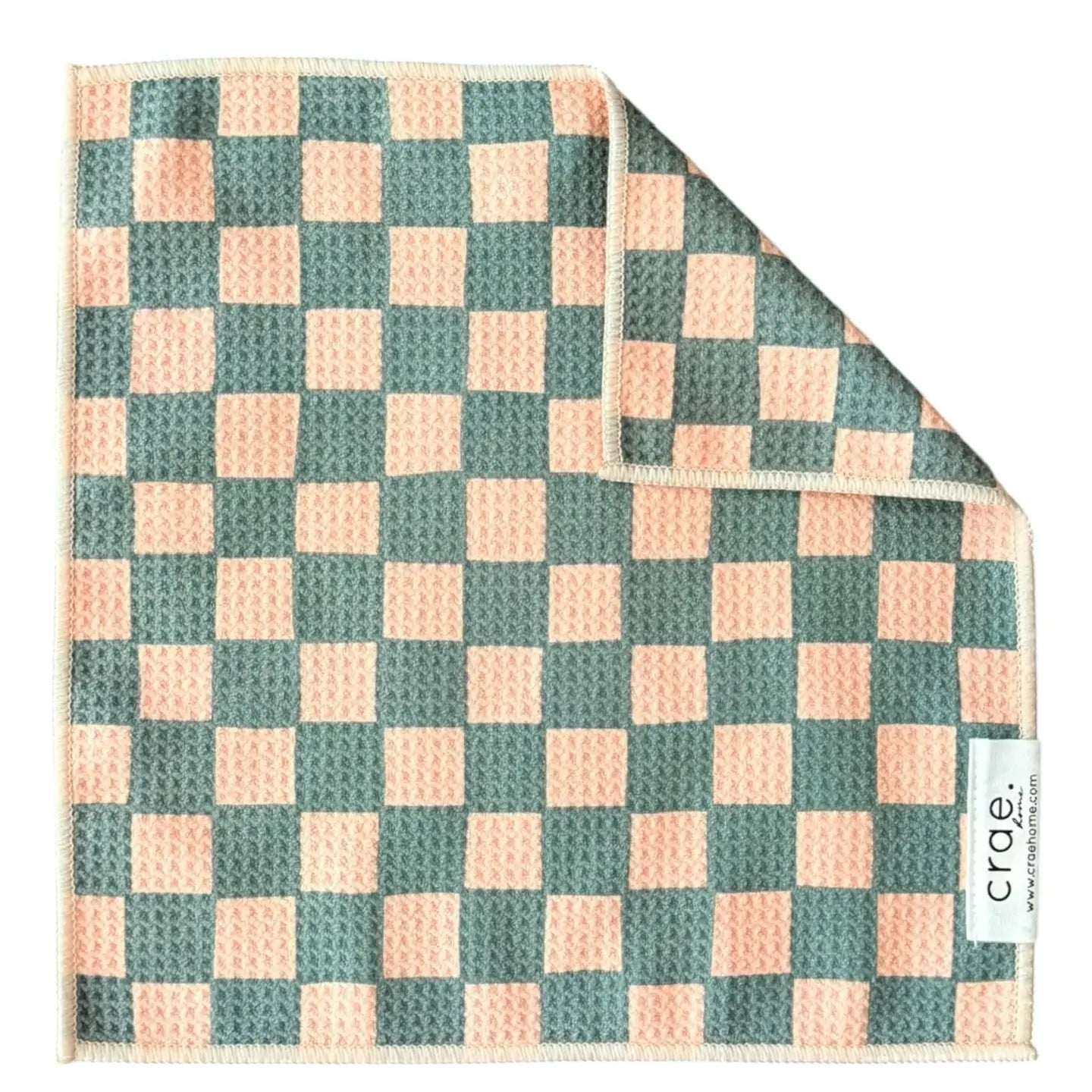 A green and peach square waffle weave microfiber washcloth with a checkerboard pattern, one corner folded over. A white fabric label with the brand name "Faire" is stitched on the edge.