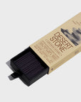 A beige box labeled "Desert Stone" from Faire’s Low Smoke Incense reveals black incense sticks, made from natural ingredients, partially slid from a black inner tray. The minimalist packaging features subtle cloudy designs and clean text.