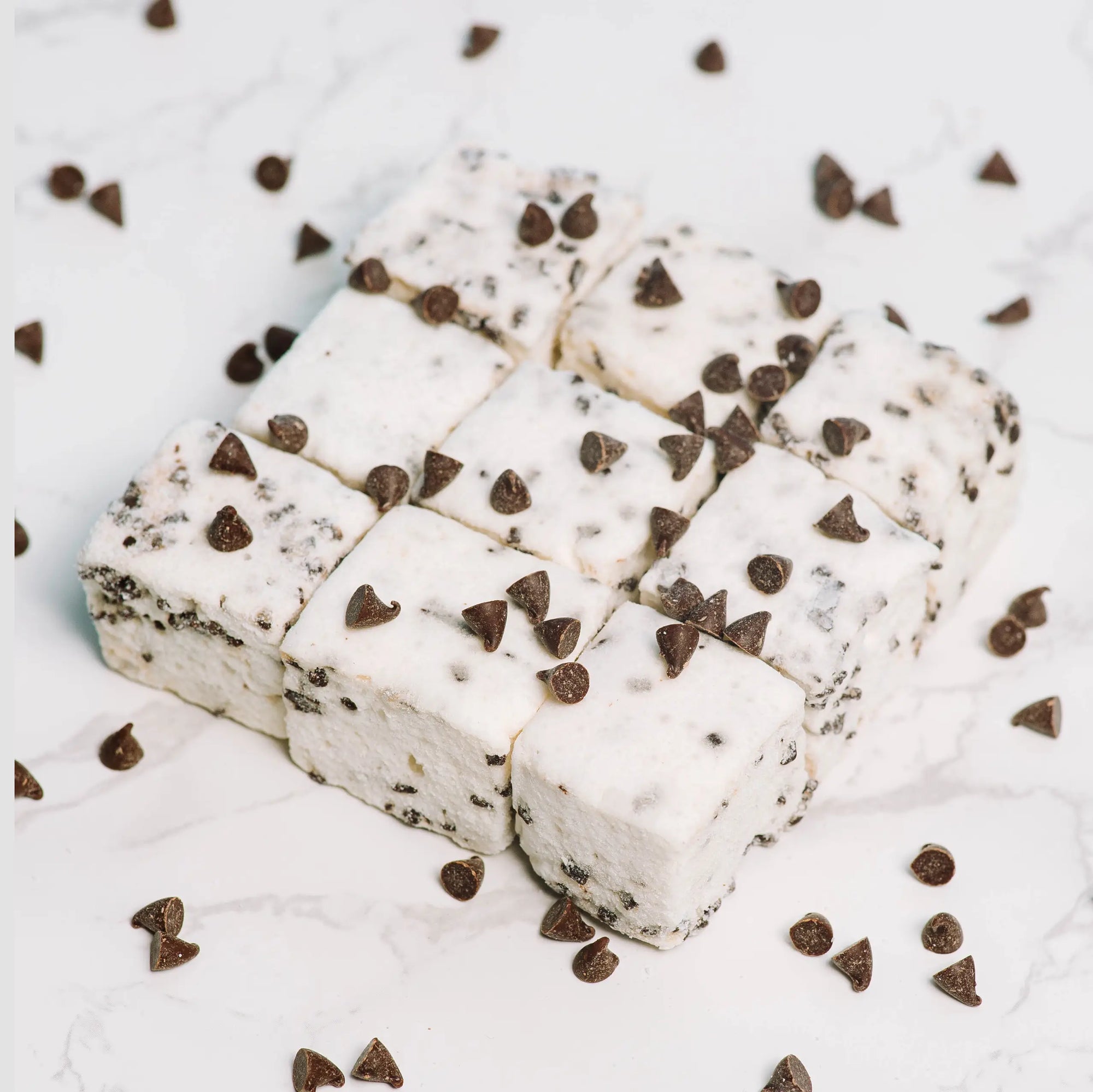 Nine square Faire Choc Chip Marshmallows, studded with chocolate chips and arranged on white marble with extra chips scattered around, make a delicious dairy-free, allergy-friendly treat.