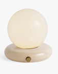 The Valencia Portable Light by Faire is a minimalist lamp with a round, frosted glass globe on a smooth, oval beige base and a small brass knob on the front.