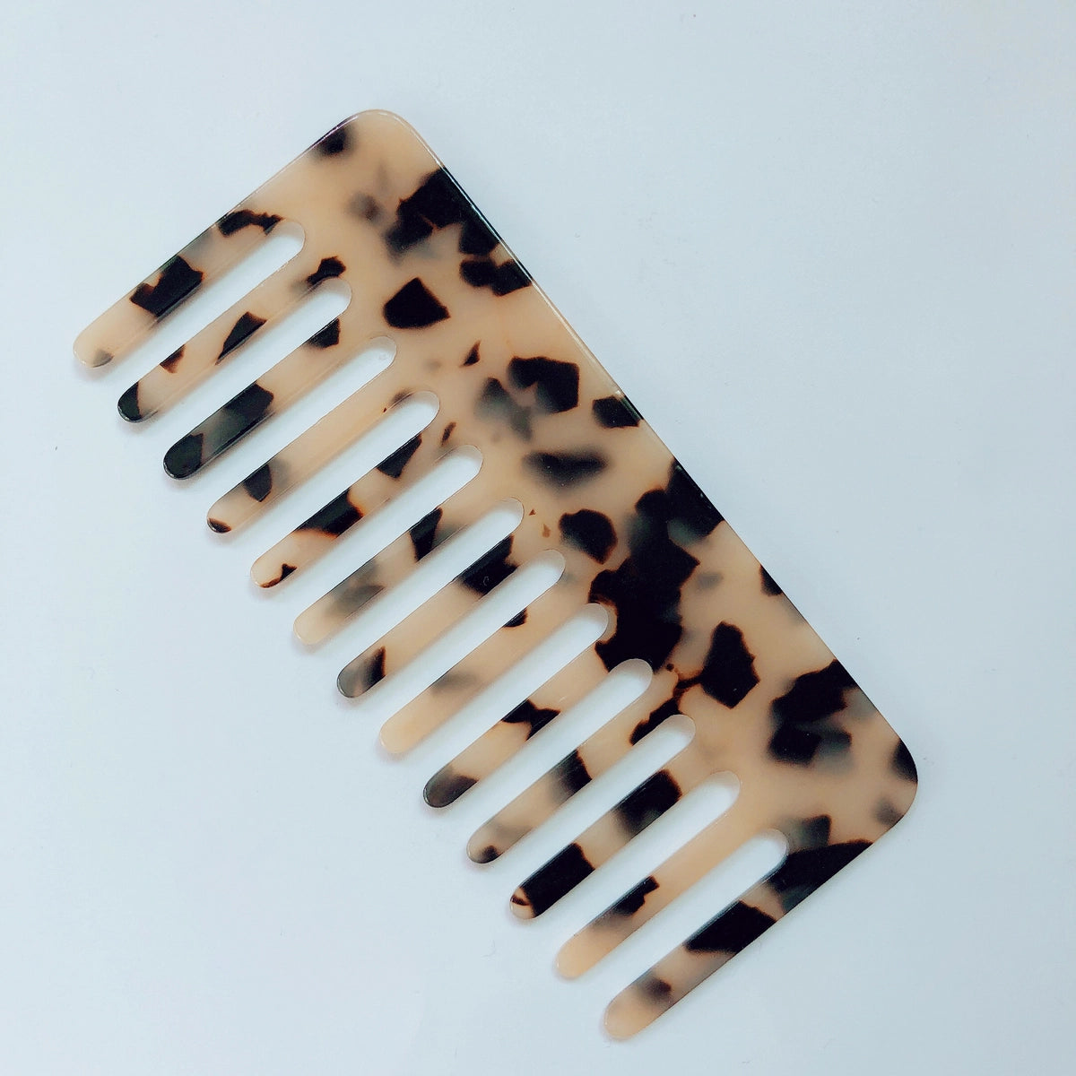 The Faire Hair Comb Assorted is a medium acetic acid comb with a tortoiseshell pattern in brown and black on beige, displayed on a plain white surface.