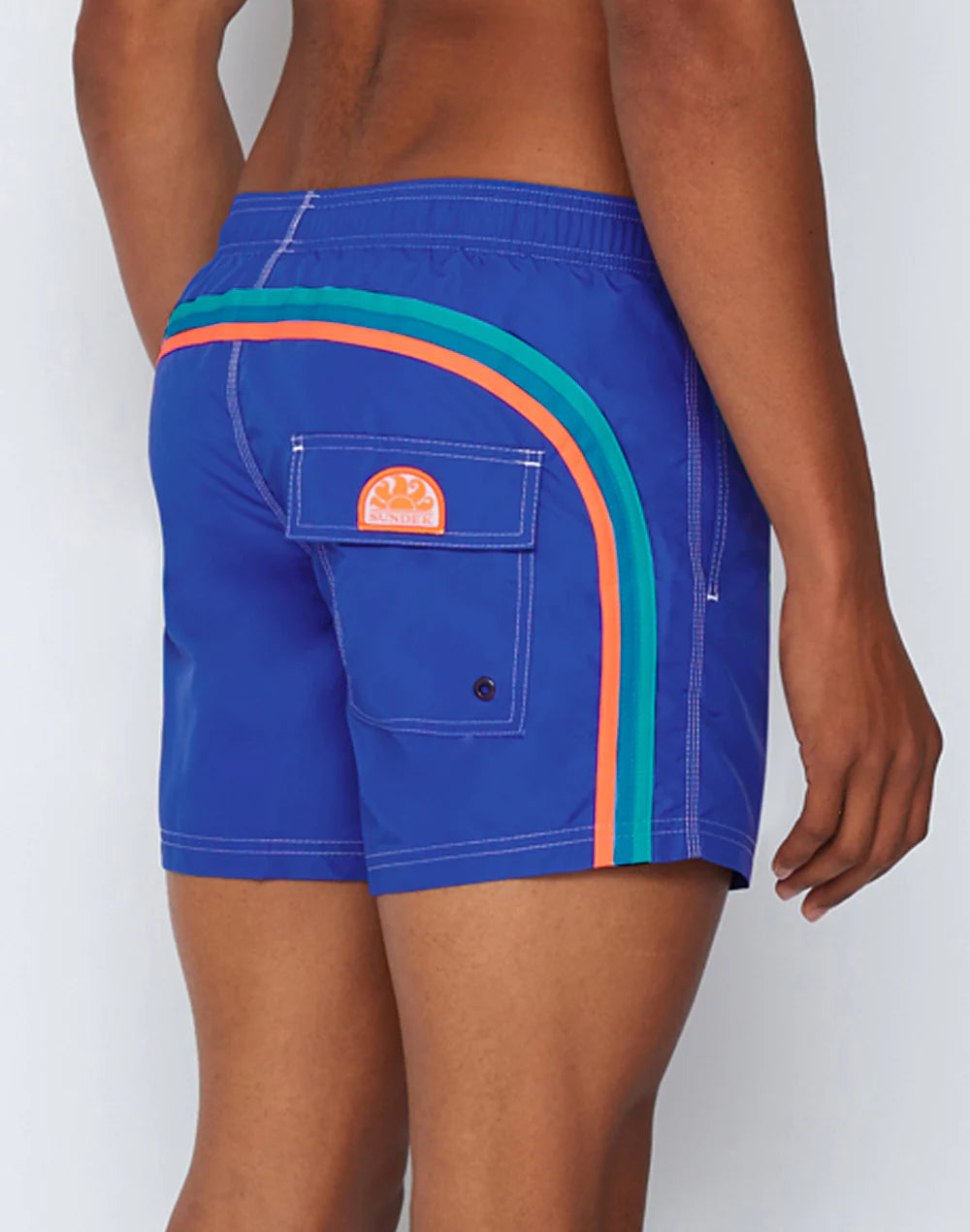 Someone models the SUNDEK/KickoffUSA ELASTIC WAIST Board Short in blue nylon-taffeta, accented with teal and orange stripes and a back pocket featuring a round logo. The image displays the shorts from side and back views.