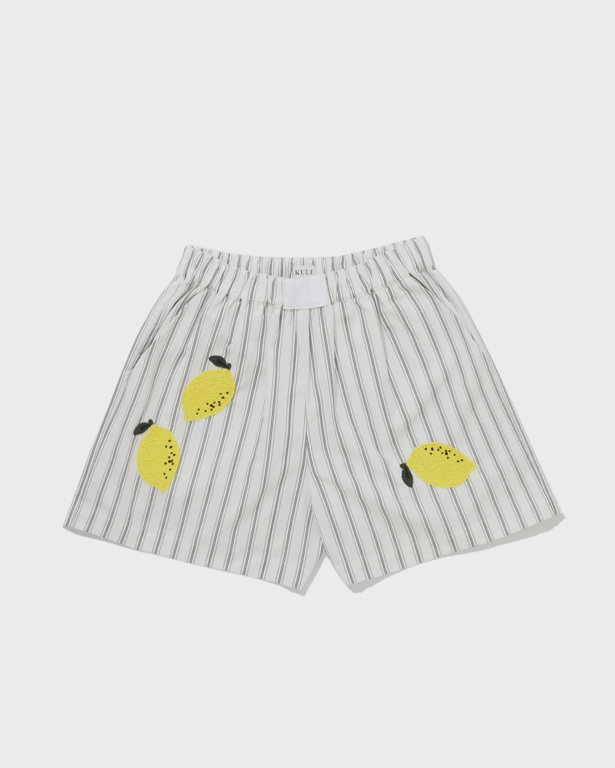 Kule's The Limon shorts feature white and gray vertical stripes, an elastic waistband, and three playful lemon appliqués with green leaves on the front—a fun nod to the Amalfi Coast.