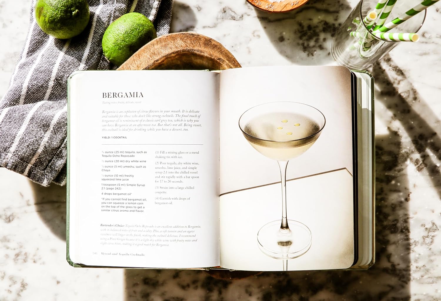 Cocktail recipe book on marble with limes and straws, Harper Collins, perfect for home bar styling.