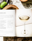Cocktail recipe book on marble with limes and straws, Harper Collins, perfect for home bar styling.