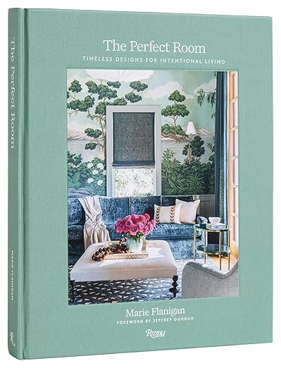 Cover of the book "The Perfect Room" by Random House. It showcases a stylish room with detailed architecture, a nature-themed wall mural, a window dressed in a blue shade, and a white coffee table decorated with flowers next to a cozy sofa wrapped in a blanket.