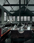 A modern living room with dark walls and floors, two black leather sofas, a central fireplace, large windows with blinds, and chic décor echoing the style of Architectural Digest at 100 by Hachette Book Group. Text appears along the left edge.