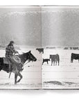 A black-and-white photo from "A Ranch Year" by Ingram Book Company shows a cowboy on horseback herding cattle in snowy Wyoming, with mountains in the background—a vivid scene of American West ranch life.
