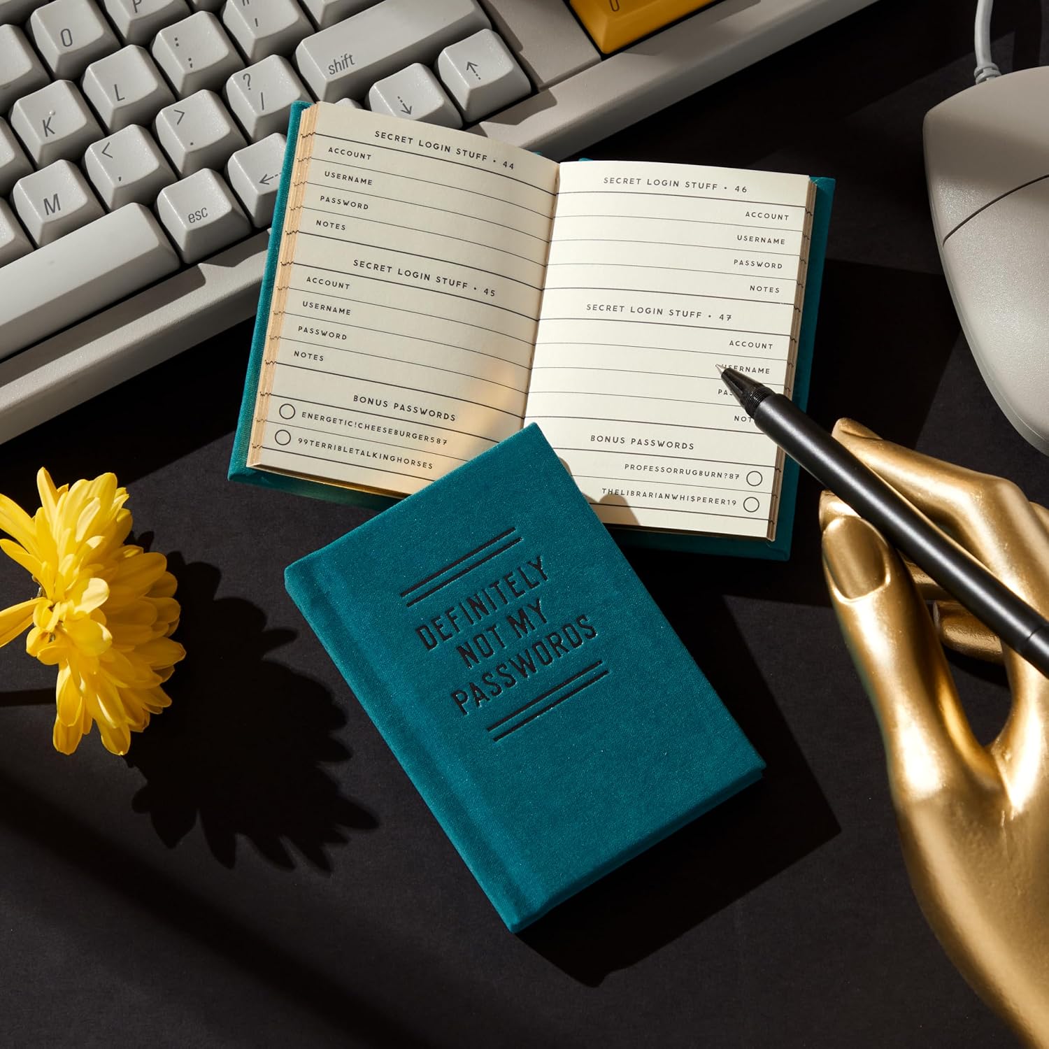 Teal Definately Not my Passwords Tiny notebook by Hachette Book Group open on desk beside keyboard and flower.