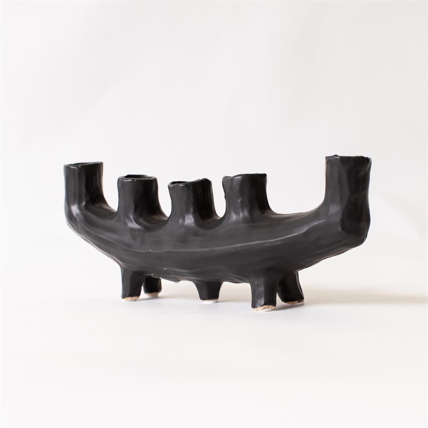 The Faire Black Crescent Shape is a sculptural, matte black ceramic candle holder with five uneven cylindrical slots and four short legs, shown against a plain white background.