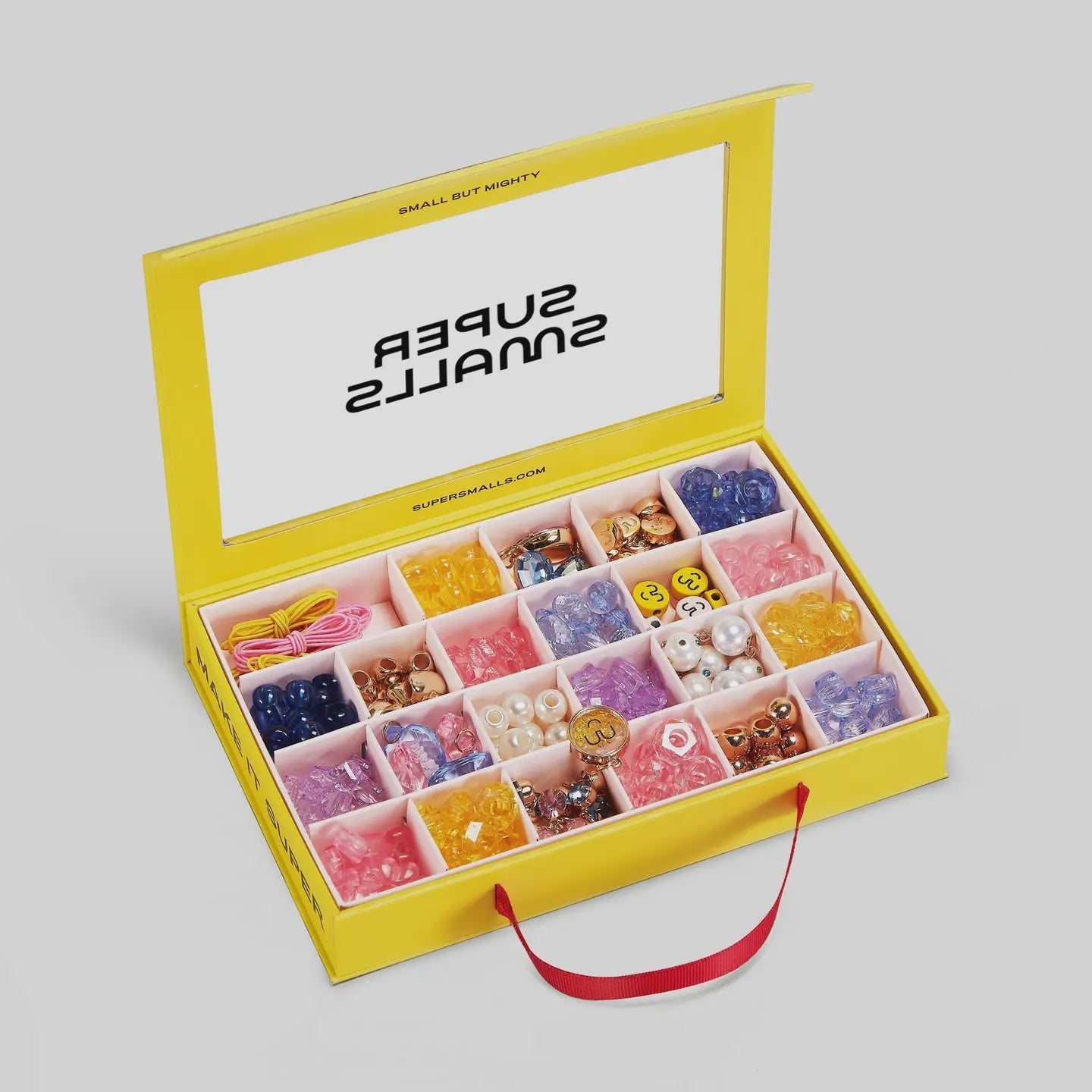 The yellow box with a red handle, titled "Make It Super DIY Bead Kit" by Faire, is filled with colorful beads and accessories neatly organized in compartments. The lid features the brand "SUPER SMALLS" printed in black.