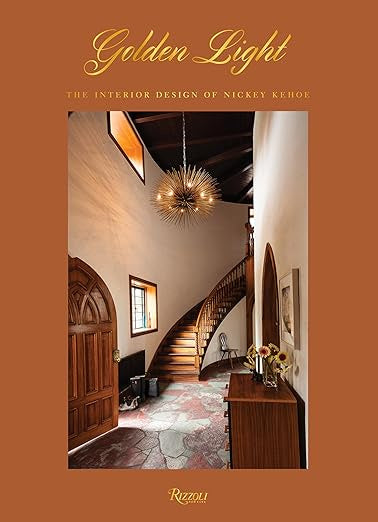 The cover of "Nickey Kehoe 9780847865260" by Random House features contemporary elegance in a grand hallway highlighted by a spiral staircase, an ornate light fixture, and wooden doors. The warm, earthy tones present reflect the signature style of Nickey Kehoe.