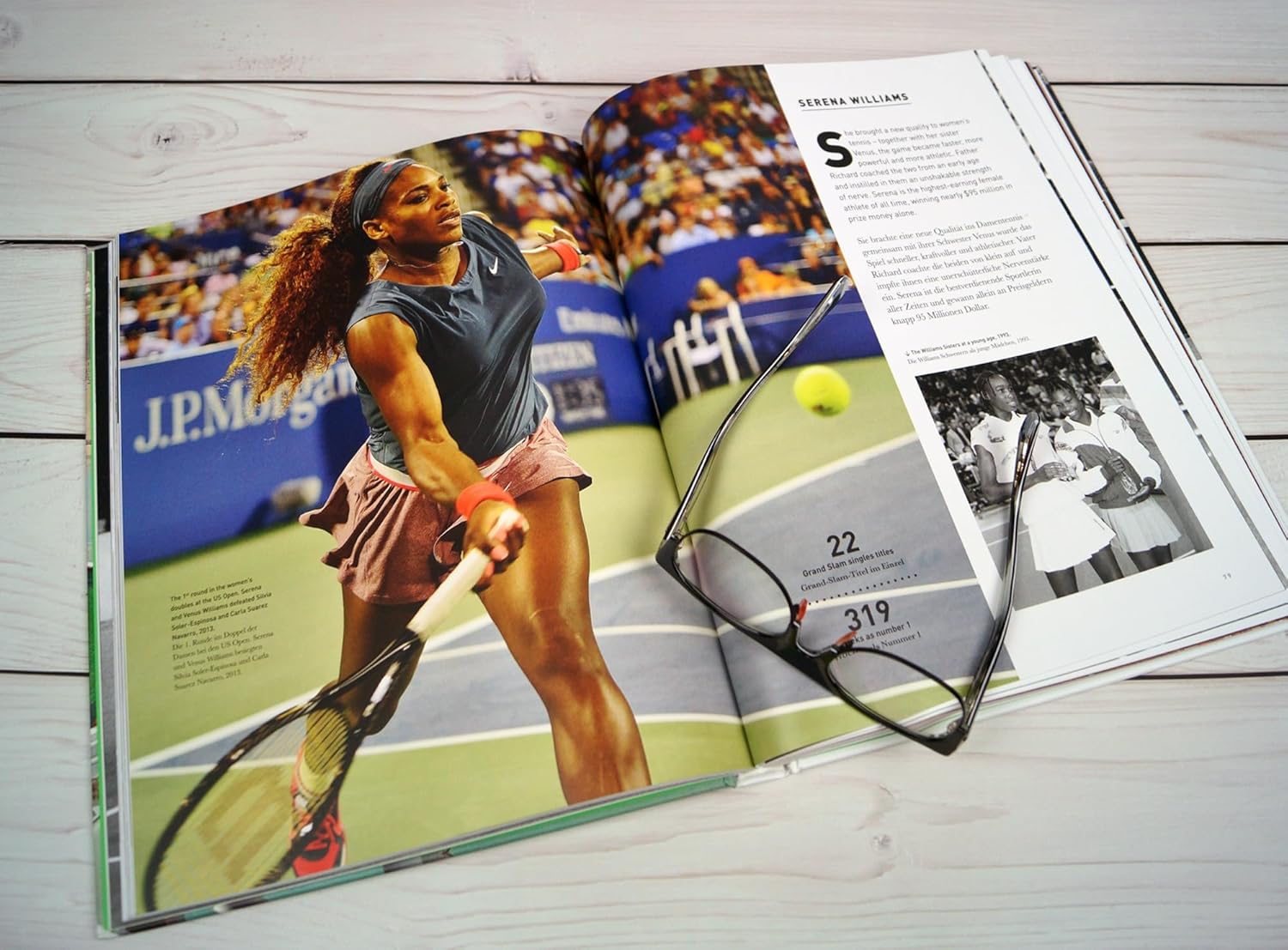 Tennis The Ultimate Book by Random House lies open, featuring a vivid forehand photo and historic black-and-white images—eyeglasses atop—making it an ideal coffee table piece for tennis enthusiasts and history lovers.