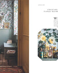 A vintage-inspired bathroom from "A Year in the French Style" by Random House features floral wallpaper, a compact sink, books on a bench, a patterned robe on the door, and a right-side close-up of assorted perfume bottles and jars.