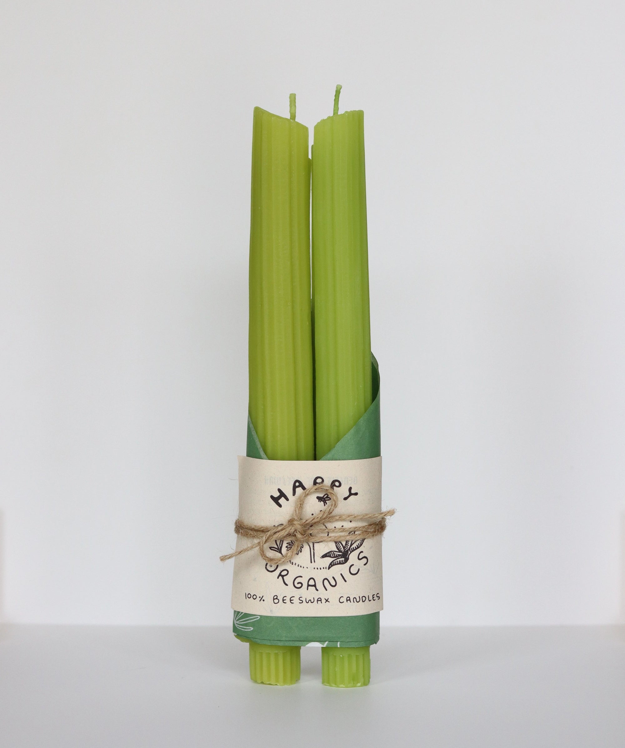 Two green Celery Beeswax Candles by Faire, wrapped with a recycled paper label reading "Faire 100% Beeswax Candles," tied with twine, and standing upright against a plain white background. Handmade in Los Angeles.