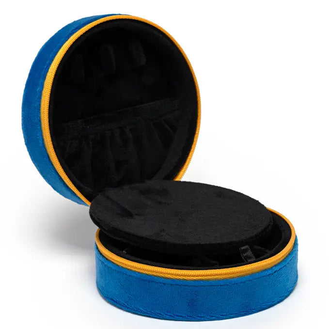 The Caviar Jewelry Case is round and blue with yellow trim, featuring a velvet exterior. It opens to reveal a black interior with compartments and an elastic pocket inside the lid.