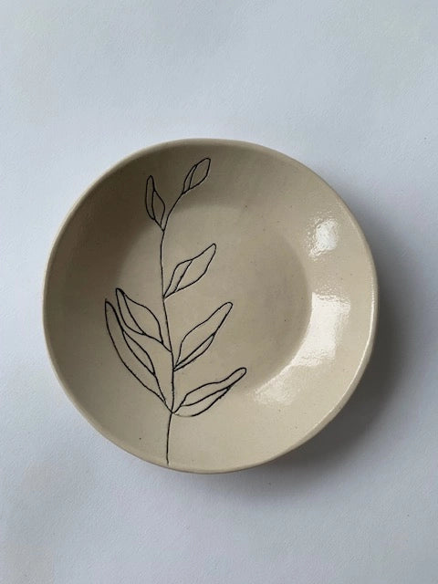 The Faire Ring Bowl is a cream-colored ceramic tray, hand-etched with a simple black leafy branch design—perfect as a jewelry catch-all. Photographed on a plain white background.