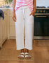 A person stands in a kitchen with hands in their pockets, wearing Frank & Eileen's Penny Sweatpant. Only their lower half is visible; they're also sporting white sandals and a pink-and-white striped top.