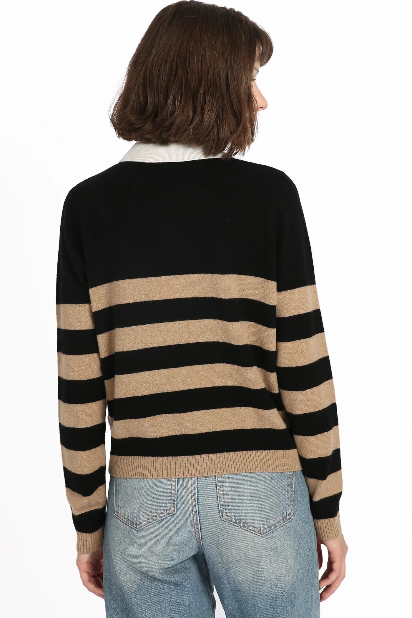 A person with shoulder-length brown hair is facing away, wearing a Rugby Stripe Polo by Minnie Rose along with light blue jeans. Ideal for casual and semi-formal occasions, the black and tan stripes stand out against the plain white background.