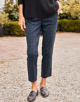 A person stands outdoors on a gravel path, wearing Frank & Eileen’s WICKLOW The Italian Chino in Italian Performance Twill, paired with a black sweater and loafers. Only their lower half is visible, with shrubs and plants in the background.