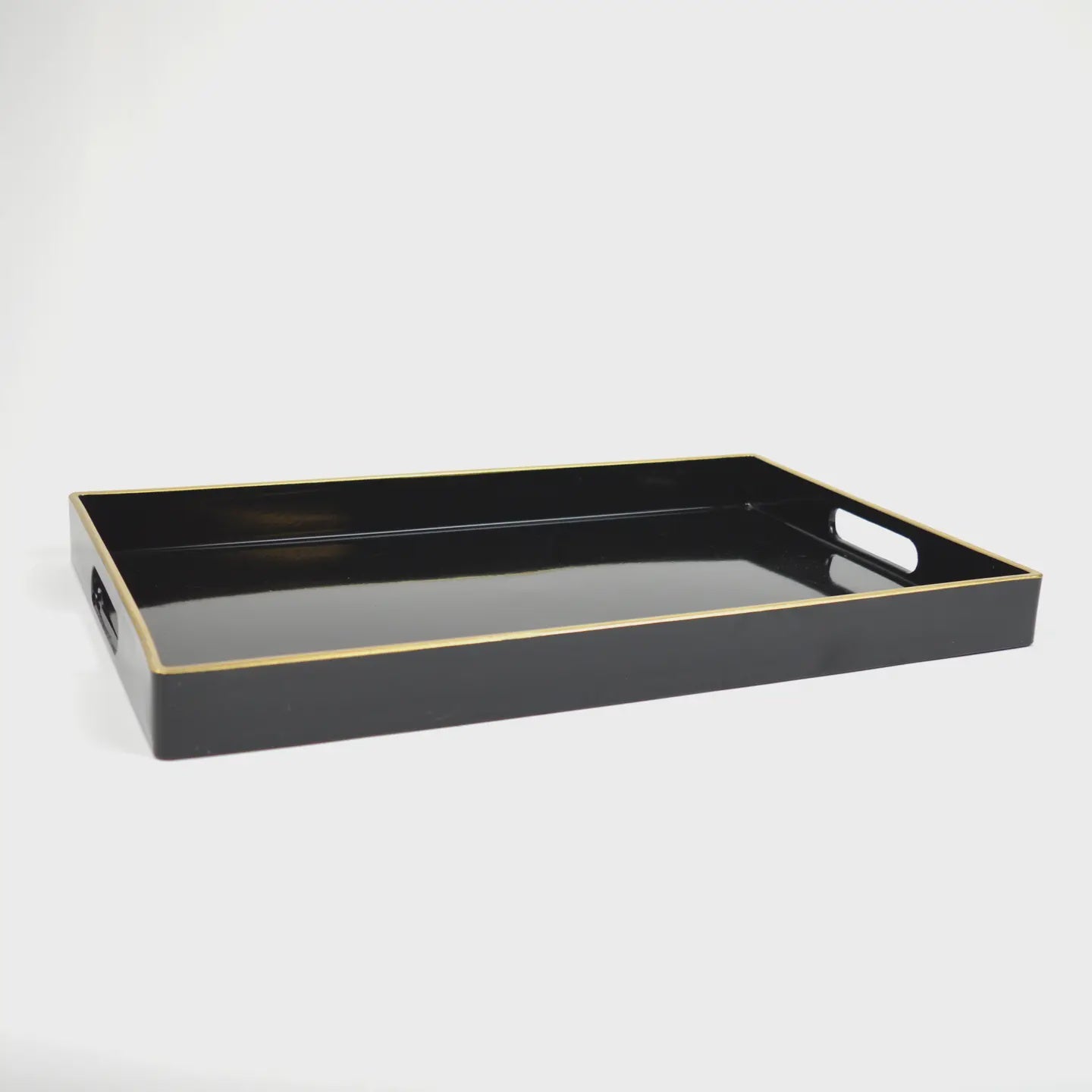 The Black Rectangular Tray by Faire showcases exquisite resin craftsmanship with a glossy finish and gold-trimmed edges. This sophisticated piece is designed with cut-out handles on both sides and is beautifully highlighted against a plain white backdrop.