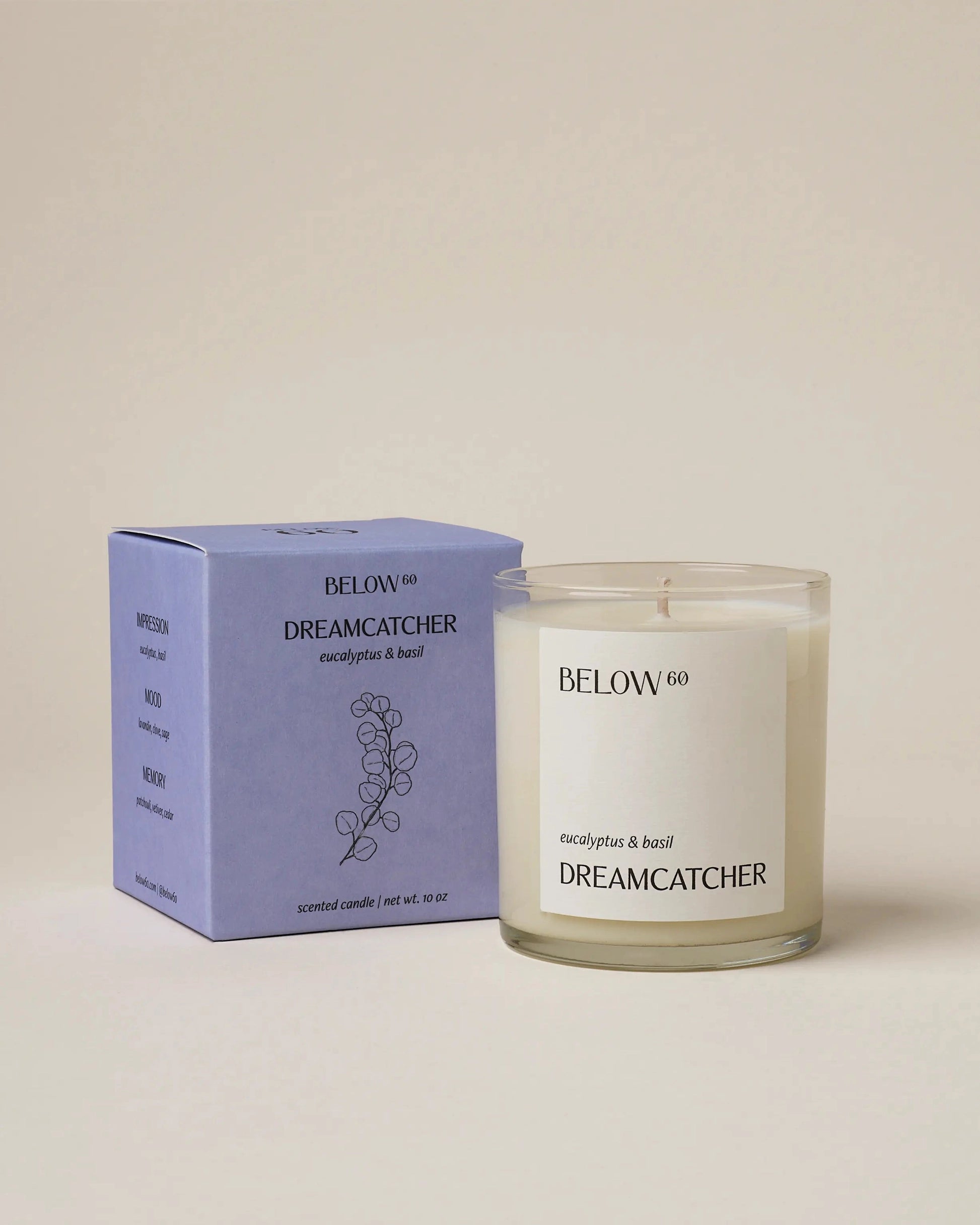 A Below 60 Candle by Faire, labeled "DREAMCATCHER eucalyptus & basil," sits next to its matching light purple box, both featuring a paraffin-free soy wax formula and a minimalist eucalyptus line drawing.