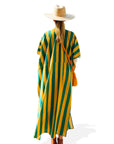 A person wearing a wide-brimmed hat and a loose Faire Surf Stripe Kaftan stands facing away, with a brown crossbody bag and brown shoes, against a white background.
