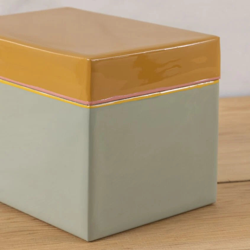 The Be Home Harlow Bright Recipe Box features a rectangular ceramic design with a glossy mustard yellow lid, pastel pink rim, and matte light gray base—ideal for organizing recipes in your kitchen and stylishly displayed on wood.