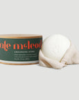 A round, white moisturizing stone infused with natural essential oils sits beside a green and orange-labeled "Grounding Stone Body Lotion" container from Faire on a light gray background.