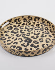 The Faire Leopard Round Tray features an elegant design, boasting a black and brown animal print pattern on a light background. It is crafted with a smooth, glossy finish and enhanced by a raised edge and built-in side handles for effortless elegance.