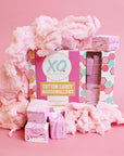 A box of Faire Cotton Candy Marshmallows, naturally colored and allergy friendly, rests on a pink surface with fluffy cotton candy and swirled pink-and-white marshmallows around it.