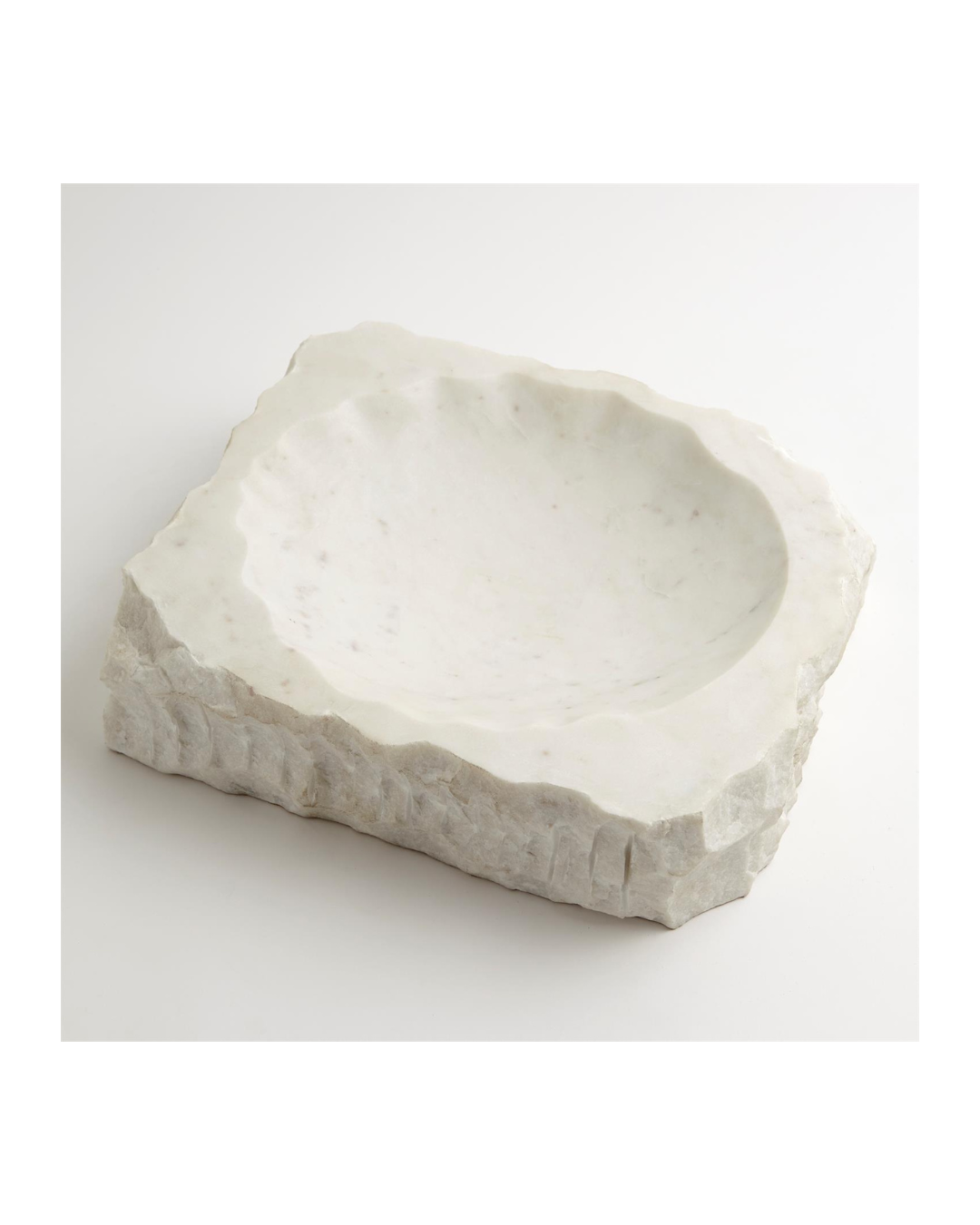 The Global Views Chiseled Block Bowl-White Marble features a white, rectangular design with a rough-hewn exterior like natural rock. Its smooth and shallow interior is ideal as a food-safe bowl for small items, elegantly resting on any white surface.