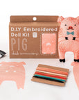 The Faire Pig Embroidery Kit is a beginner DIY set to create a cute plushie, including a box, pig outline fabric, colorful floss, stuffing, instructions, and a finished doll with a bow tie.