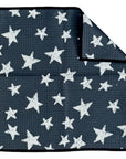 A Faire washcloth in dark gray with a textured feel, white star pattern of varying sizes, and a black border. One corner is folded to reveal the reverse side and a white "crae" tag. Made from eco-friendly materials.