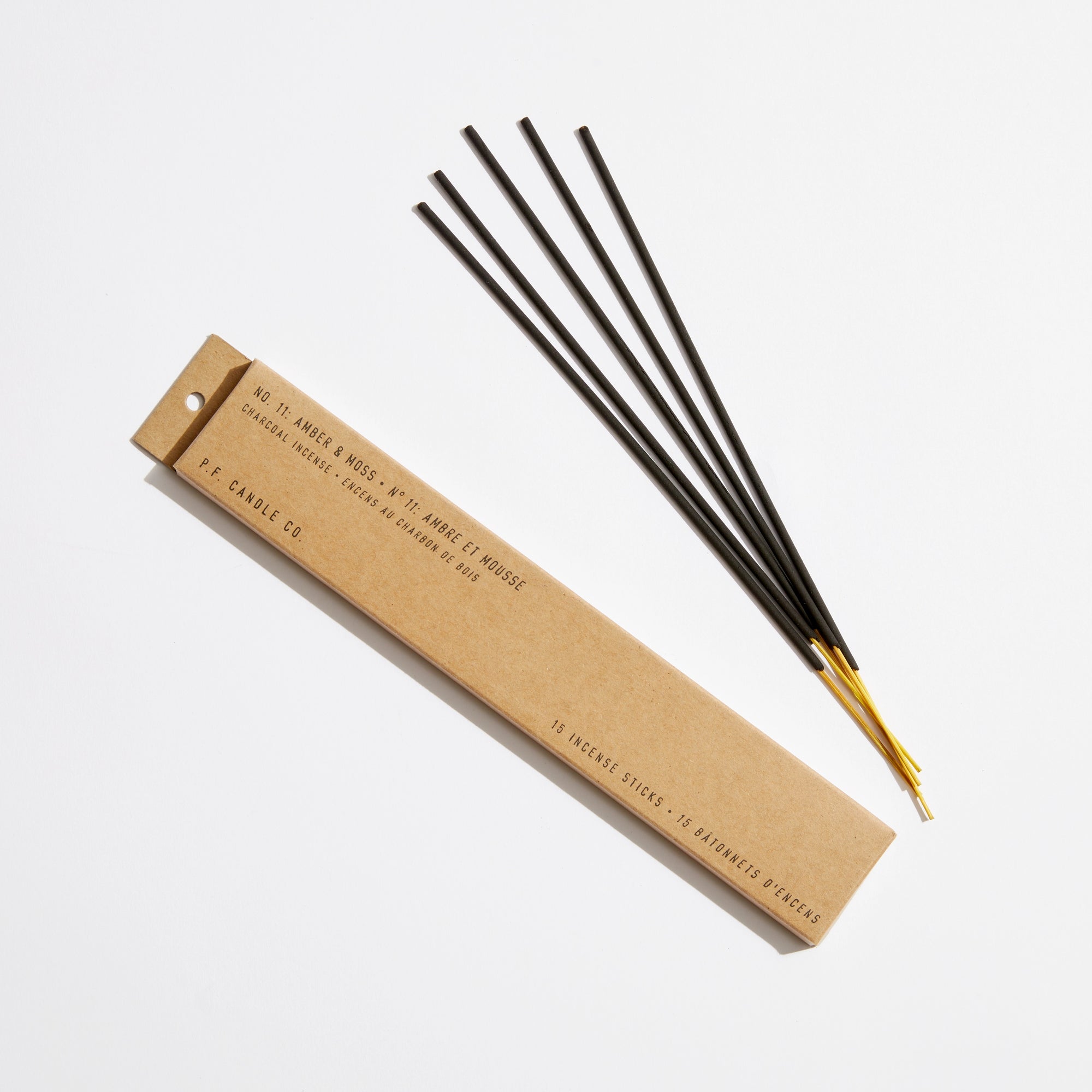 A brown rectangular box labeled "PFC Incense Sticks" by Faire rests beside four yellow-tipped incense sticks arranged in a fan shape on a white background.