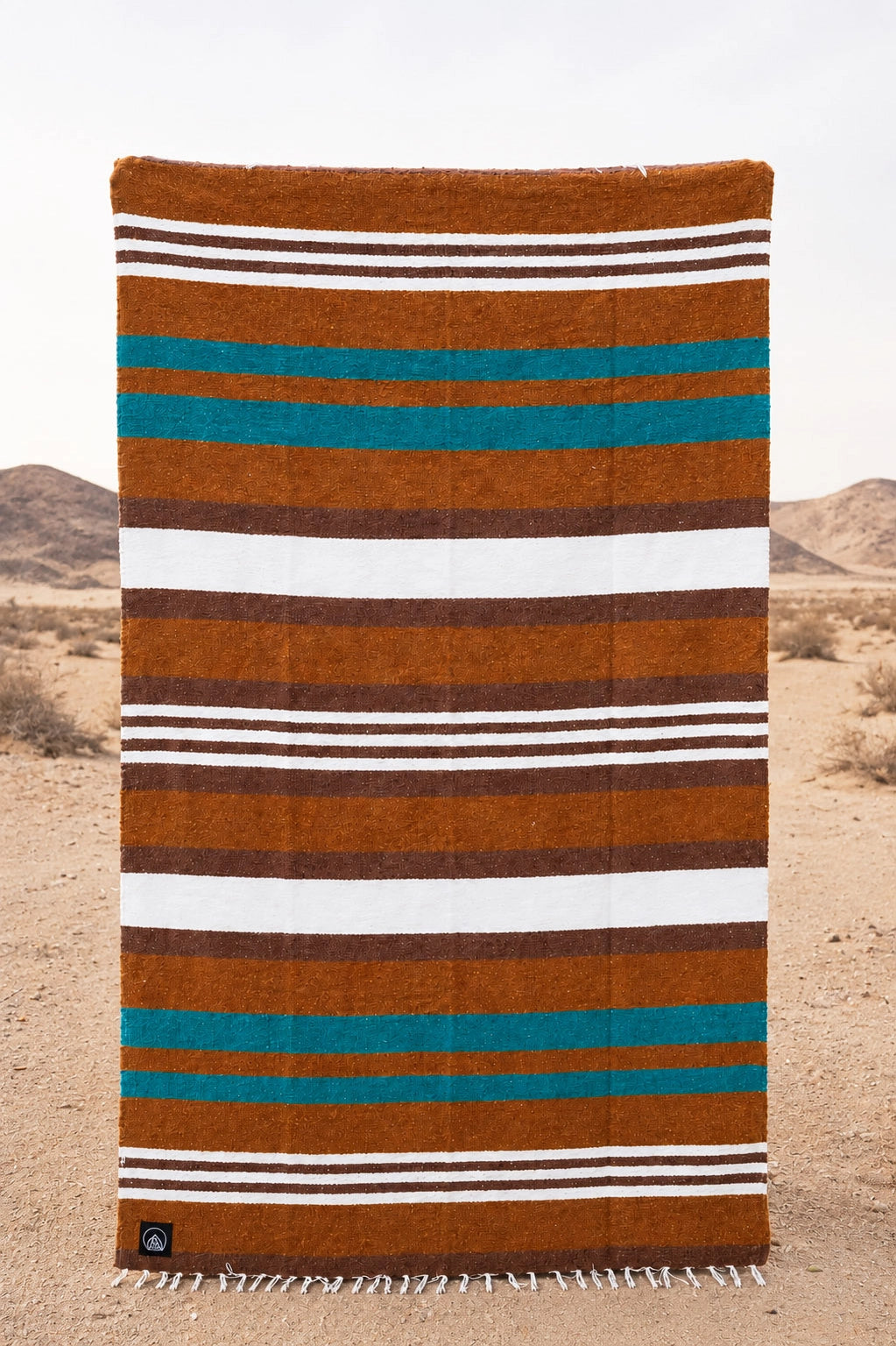 Handwoven Faire Canyon Cove blanket with brown, white, and teal stripes by Bungalow, displayed in desert landscape.