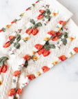 The Faire Strawberry Farm Casual Socks are cream-colored with a textured knit and embroidered red and orange strawberries plus green leaves, laid flat on a white marble surface.