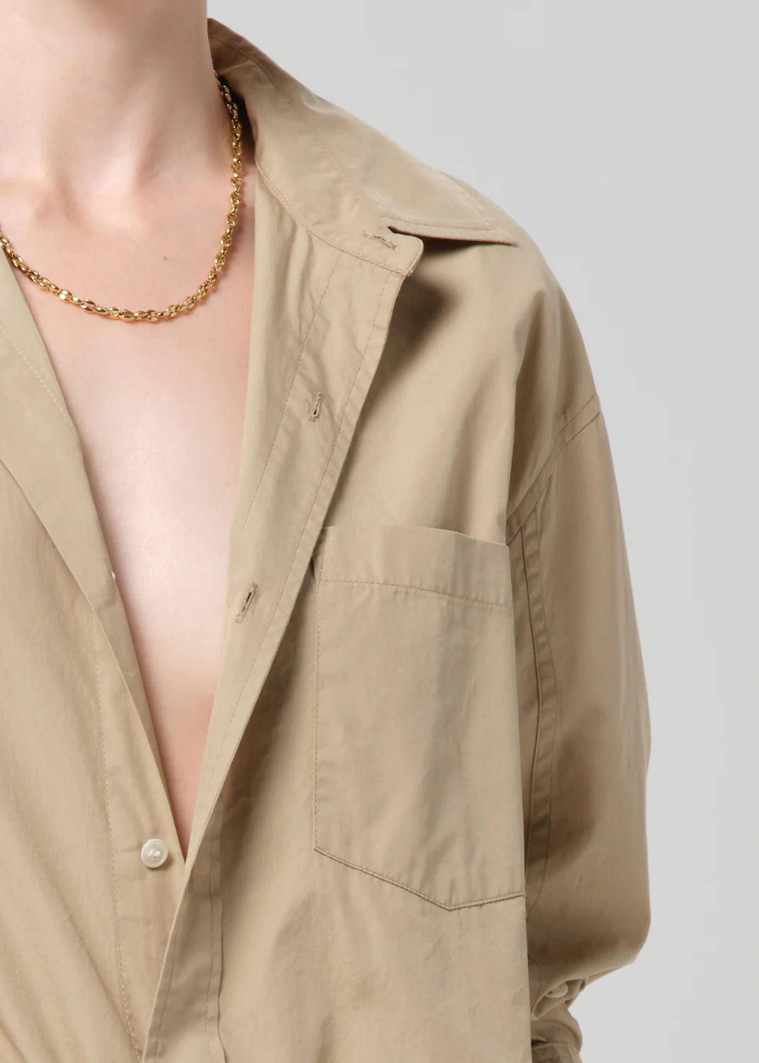 A person wears the Kayla Shirt Catalina by Citizens Of Humanity/AGOLDE, an open beige cotton poplin shirt, and a gold chain necklace, shown from shoulders to mid-chest against a plain light background.