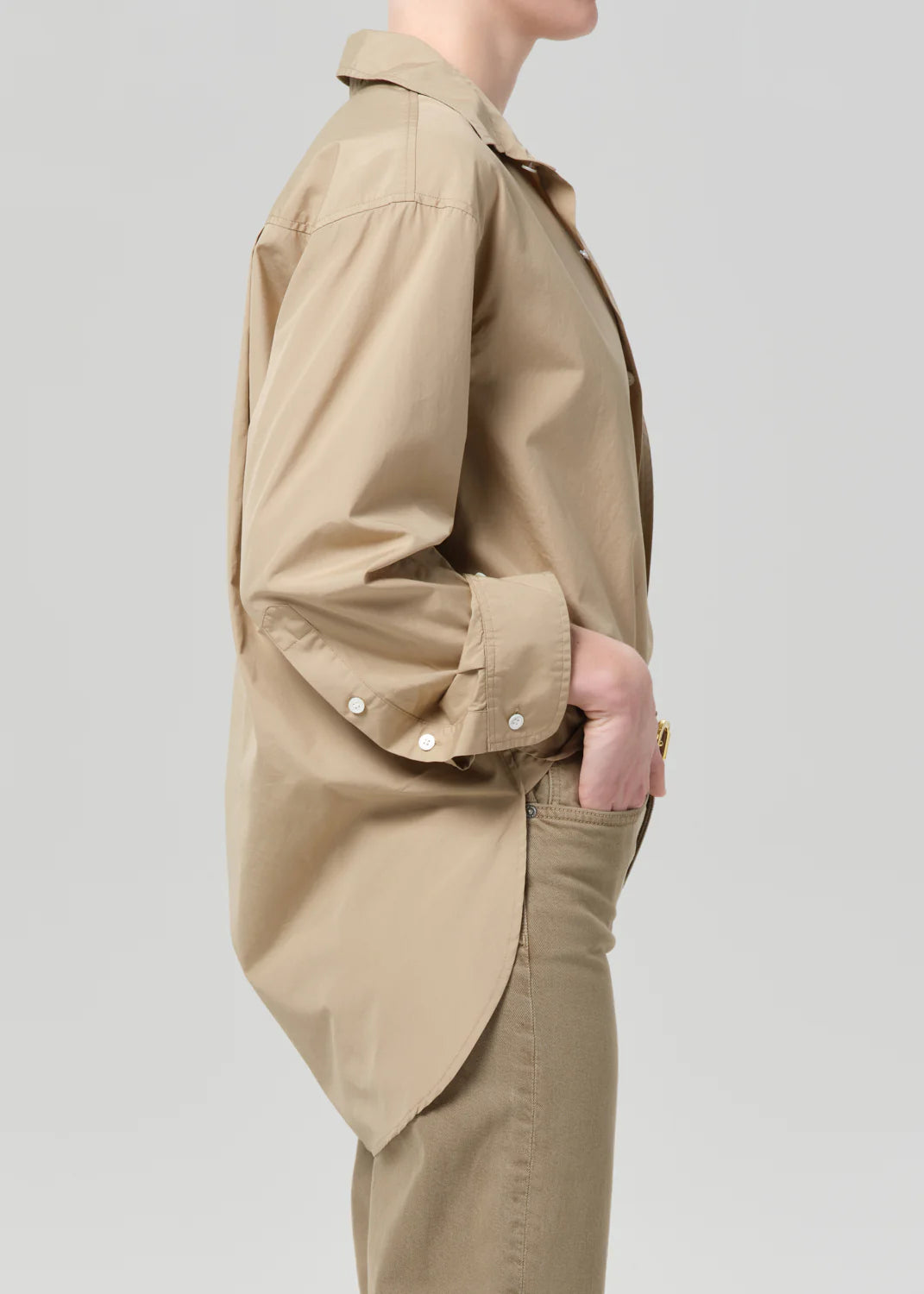 A person in profile wears the Citizens Of Humanity/AGOLDE Kayla Shirt Catalina, a loose-fitting beige poplin shirt with rolled-up sleeves, and tan pants against a plain light background.