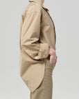 A person in profile wears the Citizens Of Humanity/AGOLDE Kayla Shirt Catalina, a loose-fitting beige poplin shirt with rolled-up sleeves, and tan pants against a plain light background.