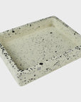 The HomArt Terrazzo Tray White is a rectangular tray with raised edges, showcasing black, gray, and quartz specks on a light beige base. It's elegantly displayed against a plain white backdrop.